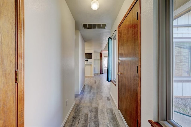 hallway with plenty of natural light, a barn door, and light hardwood / wood-style floors