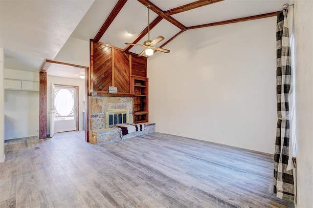 unfurnished living room with beam ceiling, wood-type flooring, a stone fireplace, and ceiling fan