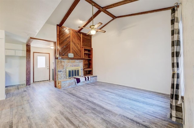 unfurnished living room featuring ceiling fan, wood-type flooring, a stone fireplace, and lofted ceiling with beams