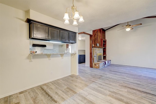 kitchen with vaulted ceiling, decorative light fixtures, a breakfast bar area, kitchen peninsula, and light hardwood / wood-style flooring