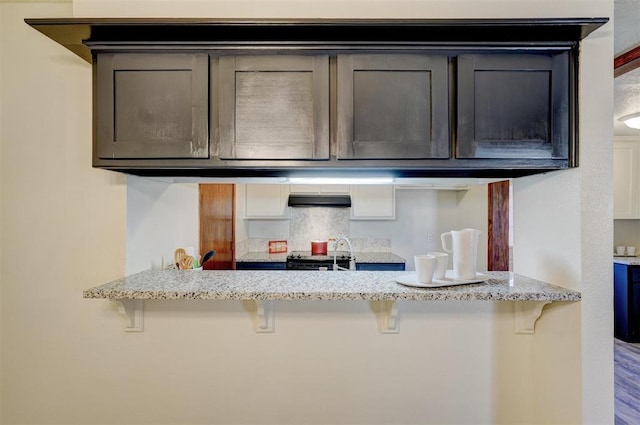 kitchen featuring light stone countertops, a breakfast bar, backsplash, and kitchen peninsula