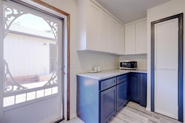 kitchen featuring white cabinetry, light stone counters, and light wood-type flooring