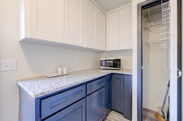 kitchen featuring blue cabinets, light wood-type flooring, white cabinets, and light stone counters