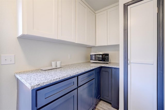 kitchen featuring white cabinetry, blue cabinets, and light stone counters