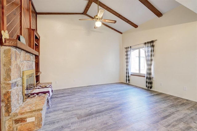 unfurnished living room featuring wood-type flooring, a stone fireplace, and beam ceiling