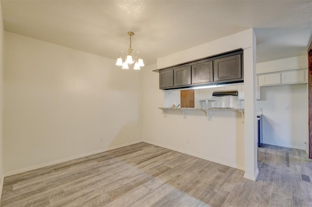 kitchen with dark brown cabinets, kitchen peninsula, light hardwood / wood-style floors, and hanging light fixtures