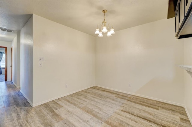 empty room with light hardwood / wood-style flooring and a notable chandelier