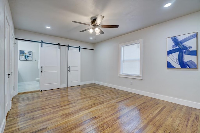 unfurnished bedroom with ceiling fan, a barn door, connected bathroom, and light wood-type flooring