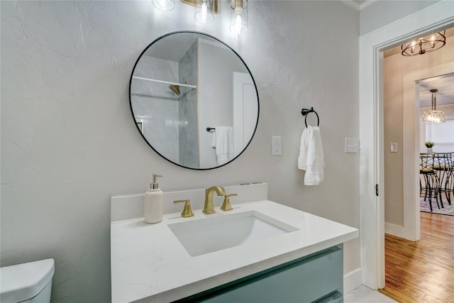 bathroom featuring hardwood / wood-style flooring, vanity, a notable chandelier, walk in shower, and toilet