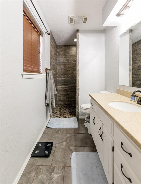 bathroom featuring vanity, a tile shower, and toilet