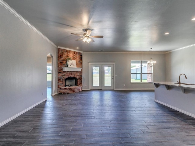 unfurnished living room featuring a brick fireplace, sink, ceiling fan with notable chandelier, and dark hardwood / wood-style flooring