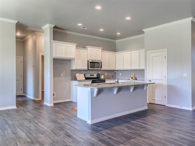 kitchen featuring appliances with stainless steel finishes, white cabinetry, a breakfast bar area, a kitchen island with sink, and light stone countertops