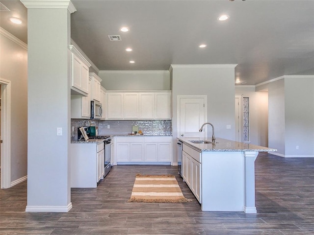 kitchen featuring sink, appliances with stainless steel finishes, white cabinetry, light stone counters, and a center island with sink