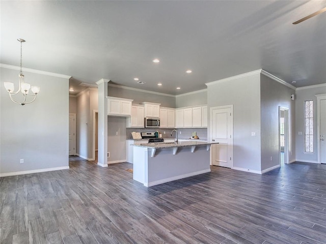 kitchen with appliances with stainless steel finishes, white cabinetry, a breakfast bar area, light stone counters, and a center island with sink