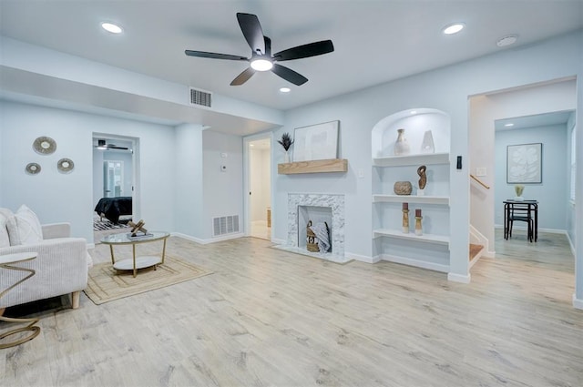 living room with ceiling fan, built in features, a fireplace, and light hardwood / wood-style flooring