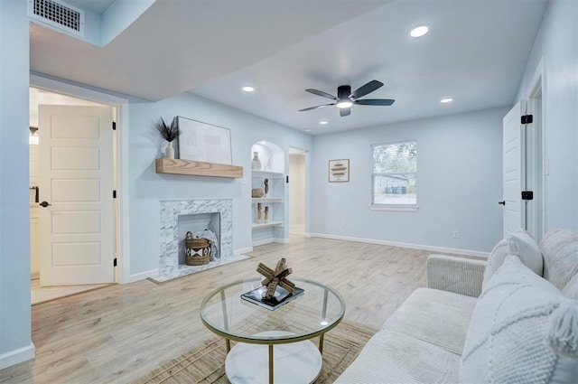 living room with a fireplace, ceiling fan, and light wood-type flooring