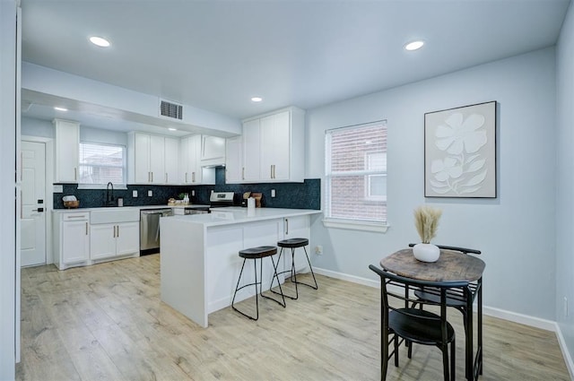 kitchen with white cabinetry, stainless steel appliances, a kitchen bar, decorative backsplash, and kitchen peninsula