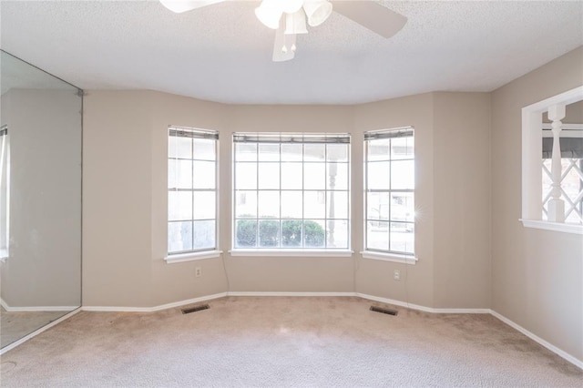 empty room with ceiling fan, light colored carpet, and a textured ceiling