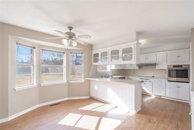 kitchen featuring white cabinetry, oven, kitchen peninsula, cooktop, and light wood-type flooring