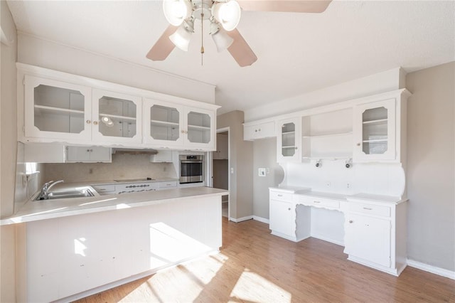 kitchen with sink, white cabinetry, stainless steel oven, light wood-type flooring, and kitchen peninsula