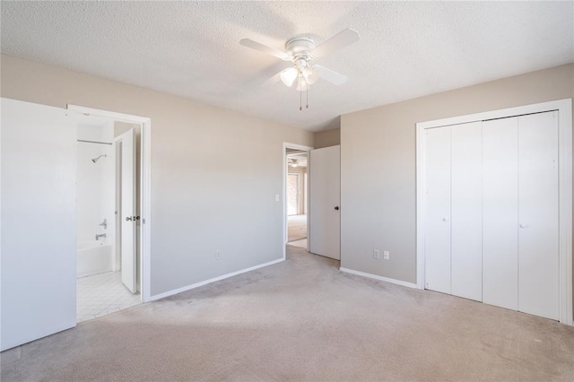 unfurnished bedroom with light colored carpet, ceiling fan, a textured ceiling, ensuite bath, and a closet