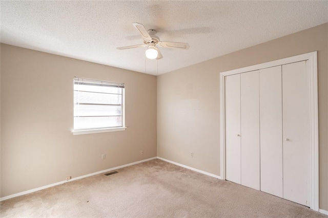 unfurnished bedroom with ceiling fan, a closet, light carpet, and a textured ceiling