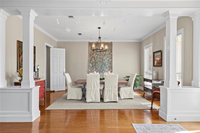 dining space featuring crown molding, wood-type flooring, a chandelier, and ornate columns