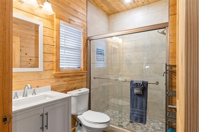 bathroom with a shower with door, vanity, wooden walls, and toilet