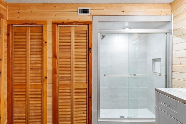 bathroom featuring walk in shower, vanity, a textured ceiling, and wood walls