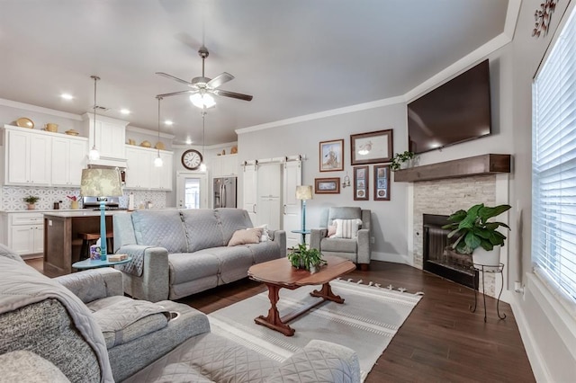 living room featuring dark wood-type flooring, ornamental molding, ceiling fan, a healthy amount of sunlight, and a barn door