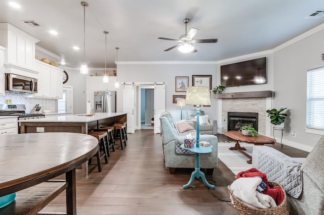 living room featuring dark hardwood / wood-style floors, ornamental molding, a barn door, and ceiling fan