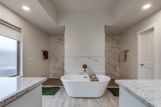 bathroom with vanity, wood-type flooring, tile walls, and a tub to relax in