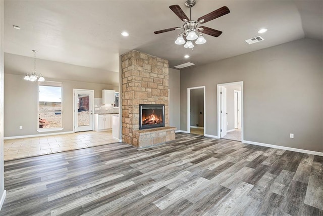 unfurnished living room featuring ceiling fan, a stone fireplace, vaulted ceiling, and wood-type flooring