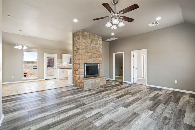 unfurnished living room featuring lofted ceiling, a fireplace, ceiling fan with notable chandelier, and wood-type flooring