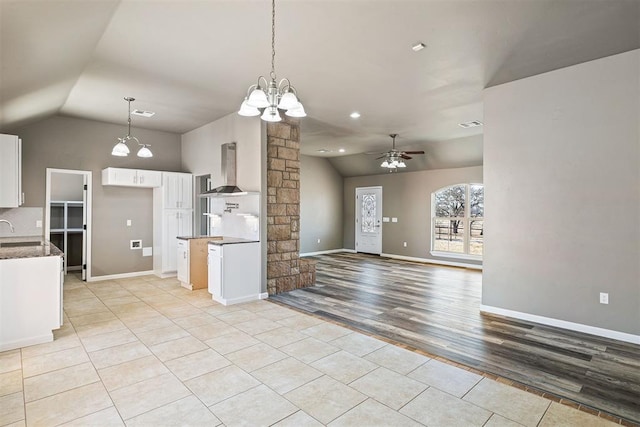 kitchen with light tile patterned flooring, decorative light fixtures, white cabinetry, sink, and wall chimney range hood