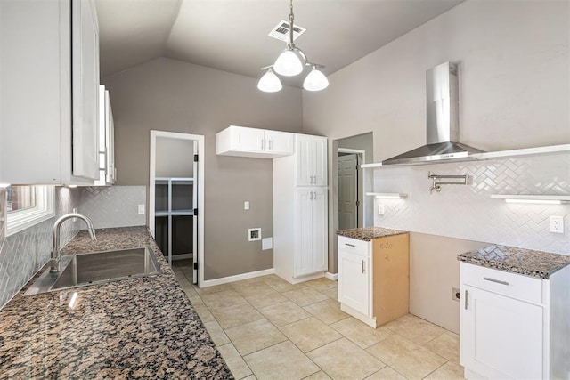 kitchen featuring wall chimney range hood, dark stone counters, sink, and white cabinets