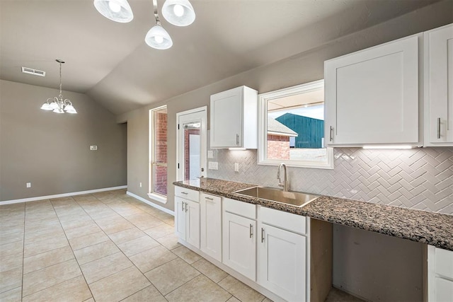 kitchen with pendant lighting, sink, white cabinetry, vaulted ceiling, and dark stone counters