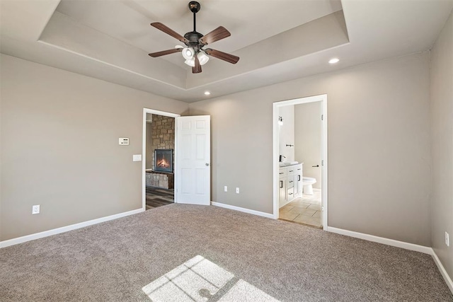 unfurnished bedroom featuring a raised ceiling, connected bathroom, light colored carpet, and a fireplace