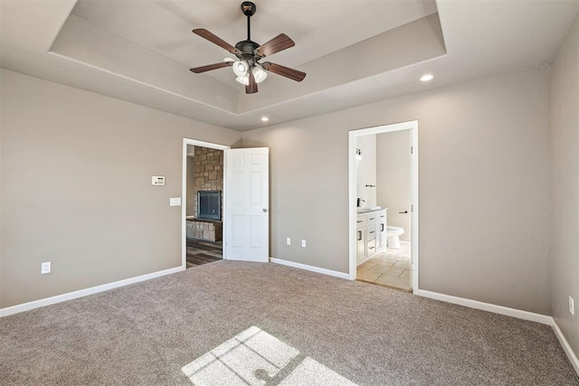 unfurnished bedroom with connected bathroom, light carpet, a fireplace, and a tray ceiling