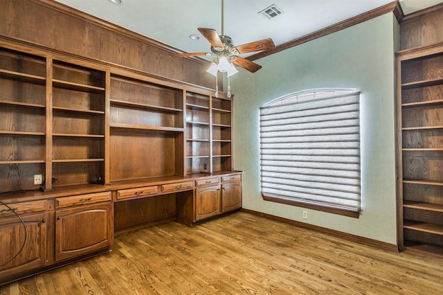 unfurnished office featuring ceiling fan, ornamental molding, built in desk, and light wood-type flooring