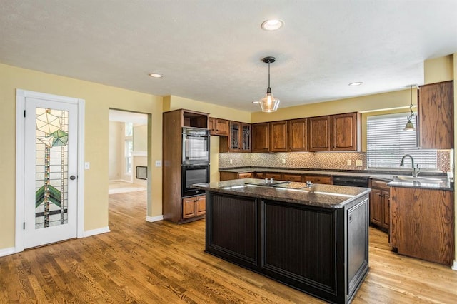 kitchen featuring double oven, backsplash, a kitchen island, dark stone counters, and light wood-type flooring