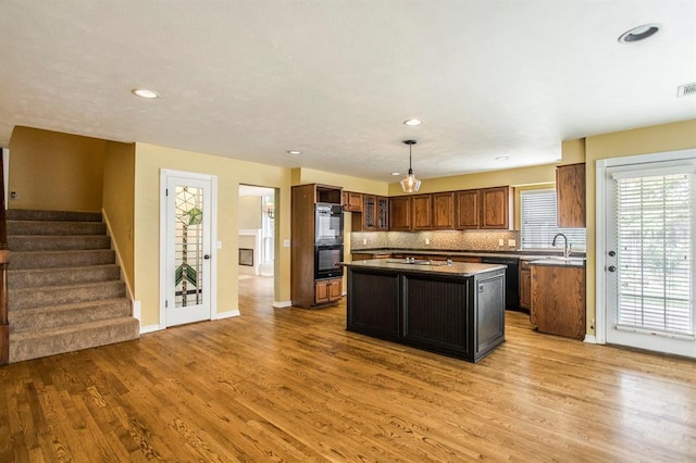 kitchen with pendant lighting, sink, light hardwood / wood-style flooring, a kitchen island, and decorative backsplash