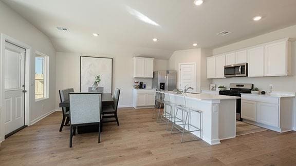 10225 NW 28th St, Yukon, OK 73099 - kitchen with white cabinetry, appliances with stainless steel finishes, a kitchen island with sink, and a breakfast bar area