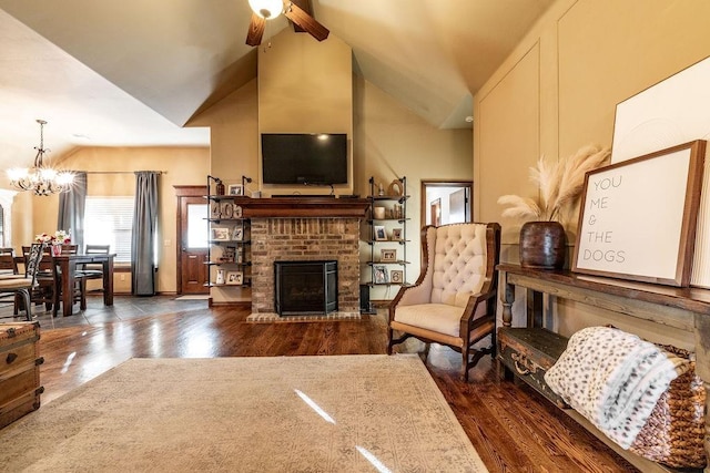 sitting room featuring dark wood-type flooring, high vaulted ceiling, a fireplace, and ceiling fan with notable chandelier