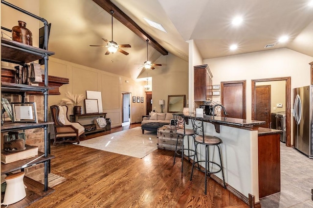 kitchen with a breakfast bar, wood-type flooring, stainless steel fridge, kitchen peninsula, and beamed ceiling