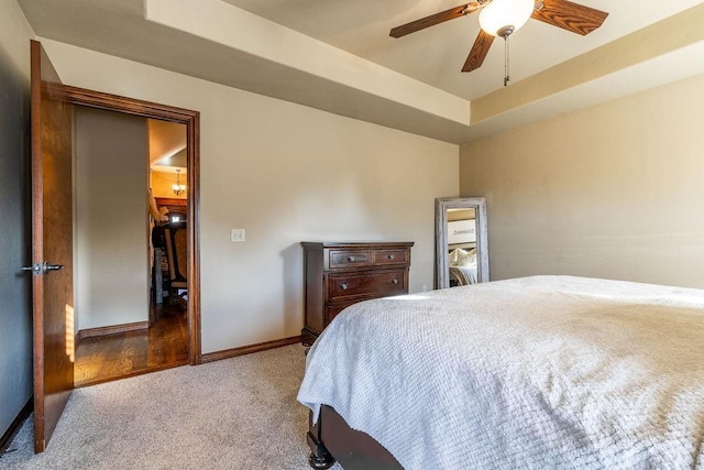 carpeted bedroom with a raised ceiling and ceiling fan