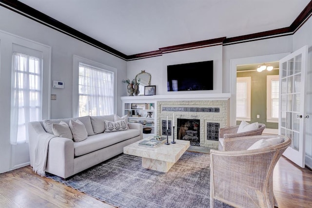 living room featuring crown molding, wood-type flooring, and a brick fireplace