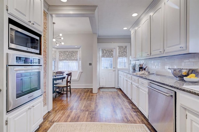 kitchen with white cabinets, decorative backsplash, ornamental molding, stainless steel appliances, and light stone countertops