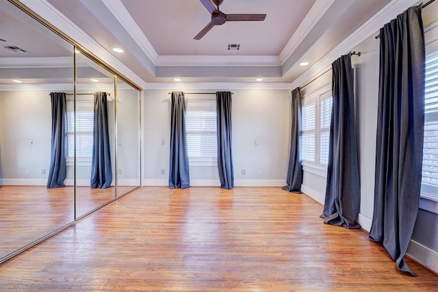 interior space with crown molding, a raised ceiling, and light wood-type flooring