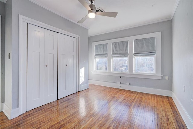 unfurnished bedroom with crown molding, wood-type flooring, a closet, and ceiling fan